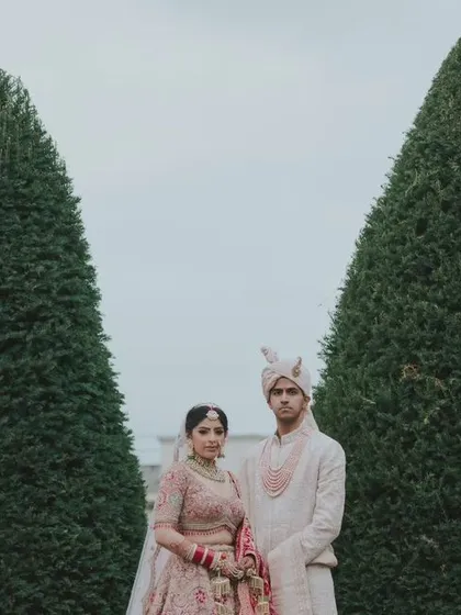 A formal, symmetrical portrait of the couple framed by perfectly manicured trees. This shot combines classic portraiture with the unique features of the wedding venue.