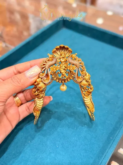 This antique-finish bajuband has a unique design with a Nagas (serpent) hood protecting the central deity motif. The single pearl drop adds a touch of elegance to this traditional armlet.