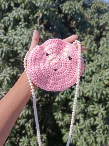 A close-up of the pink round sling purse with a pearl strap. It's a fun and stylish accessory for younger customers.