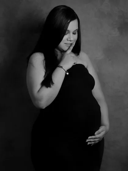 A stunning solo portrait in black and white. The simple background and classic lighting put all the focus on the mom-to-be's serene expression and the beautiful shape of her pregnancy.