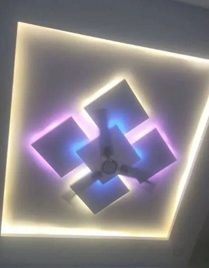 A central fan fixture is surrounded by floating squares with dual-color backlighting. The outer cove light provides a warm, uniform glow.