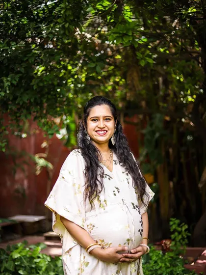 A classic solo maternity portrait that beautifully highlights the baby bump. The mother-to-be's warm smile and the lush green background create a serene and happy image, celebrating this special time in her life.