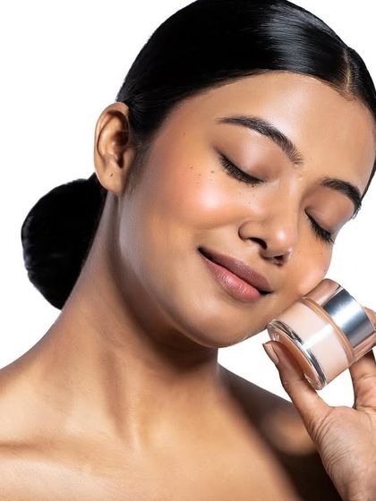 This image conveys the pleasure of using a quality skincare product. The model's relaxed expression and the way she holds the jar suggest a moment of self-care. The lighting gives her skin a beautiful, radiant finish.