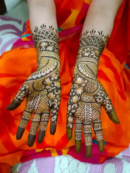 A beautiful and happy client showing her full-hand traditional mehndi. The design features lotus bands and intricate patterns that extend up the arm.