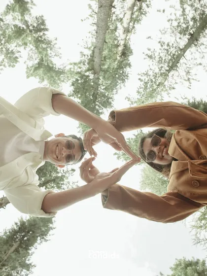A creative, low-angle shot of the couple making a heart shape with their hands against the sky and trees. It’s playful, joyful, and unique.