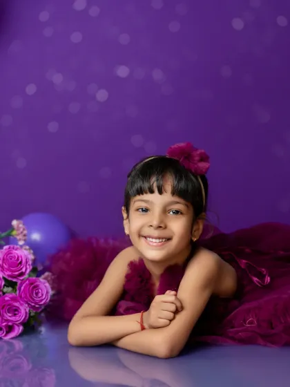 A sweet, relaxed portrait from a fifth birthday session. Her genuine smile shines against the vibrant purple backdrop.