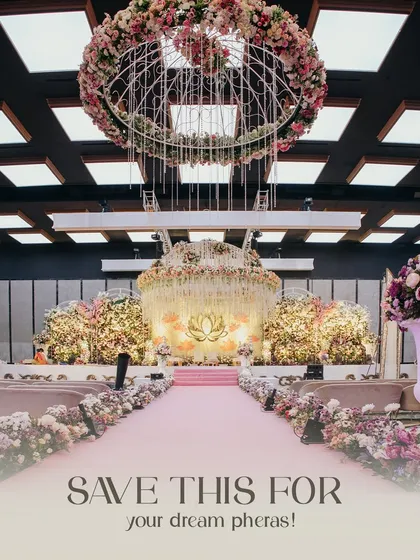 An indoor wedding setup designed for a fairytale. The aisle is lined with lush florals leading to a magnificent stage, all under a stunning floral chandelier, transforming the ballroom into a dreamscape for the pheras.