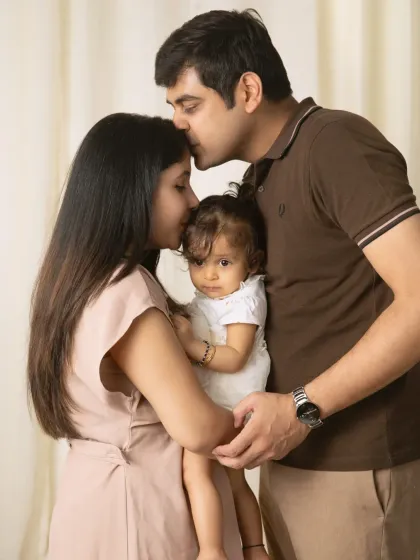 A beautiful and intimate family portrait, with both parents kissing their baby girl's head, creating a circle of love.
