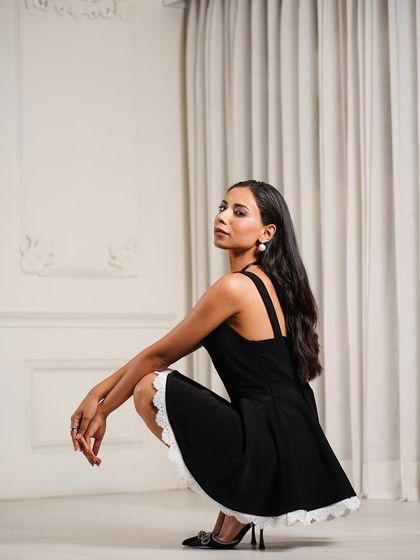 A simple yet elegant black dress with delicate white lace trim. I styled this piece with classic pointed heels for a timeless look, captured in a dynamic pose to show the garment's movement.