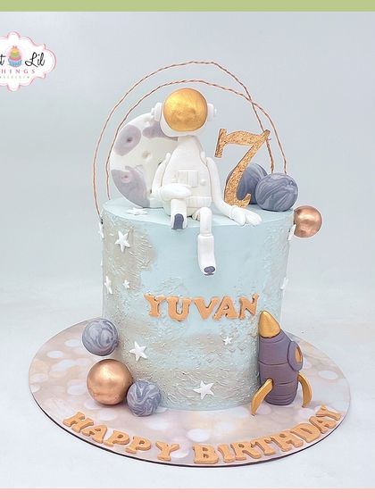 A cosmic adventure for a 7th birthday. This space-themed cake features an astronaut sitting on the moon, surrounded by planets and a rocket, all in a dreamy blue and gold palette.