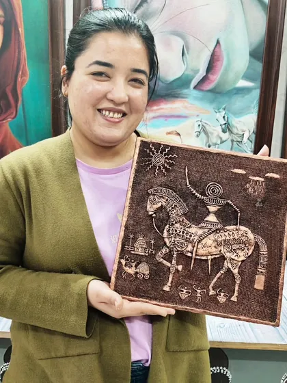 A student with her intricate relief artwork depicting a traditional Indian horse motif. This technique involves building up layers of clay to create a raised design.