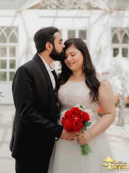 A classic romantic pose with the groom kissing the bride's forehead. The red roses add a pop of color and symbolism to this sweet moment.