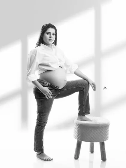 A confident and modern black and white portrait. The client's pose, with an open shirt and jeans, creates a stylish and bold image that celebrates the pregnant form.