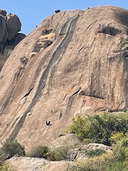 A wide view of the impressive Mahout Rock at Talai Betta, with a climber visible on one of the routes.