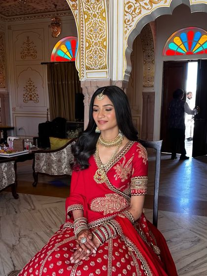 A moment of quiet reflection for the bride. The entire look, from the soft makeup to the elegant red lehenga, comes together to create a picture of serene bridal beauty.