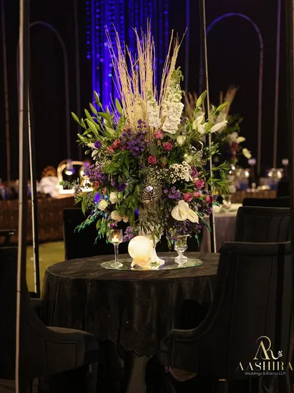 A moody and romantic tablescape, with a lush floral centerpiece on a black velvet tablecloth, surrounded by elegant black chairs.