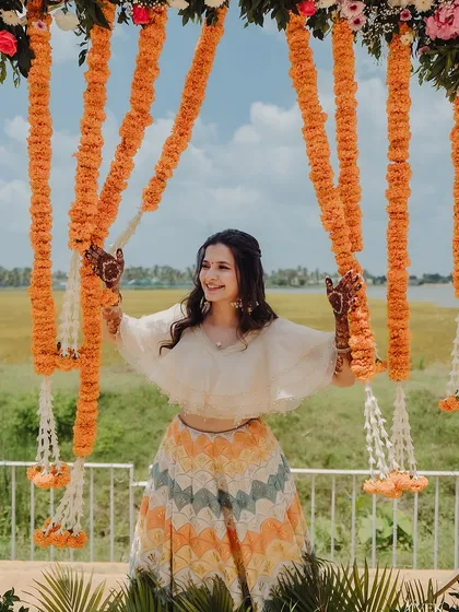 A joyful shot of a client at her outdoor mehndi event, her henna-adorned hands framed by marigold decorations.