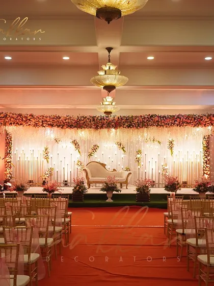 A gorgeous reception stage with hues of orange and red. The floral backdrop and candle-lit aisle create a warm, elegant, and chic atmosphere.