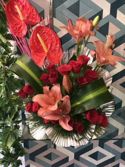 A modern table arrangement featuring exotic anthurium flowers, red roses, and lilies. This style is perfect for corporate offices or as a contemporary home decoration.