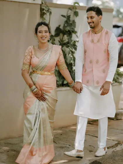 Here is an example of subtle and elegant couple coordination. The groom wears a simple white kurta and pants, elevated by a custom-made light pink Nehru jacket with delicate gold embroidery that complements his partner's saree.