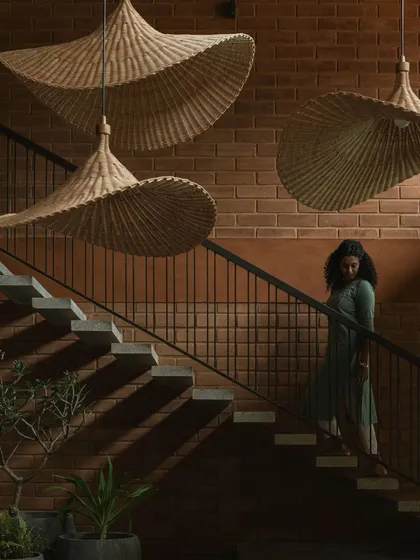 A detail of the floating staircase at Villa Maati. The design features cantilevered stone steps against an exposed brick wall, with sculptural bamboo pendant lights that create dramatic shadows and highlight the material textures.