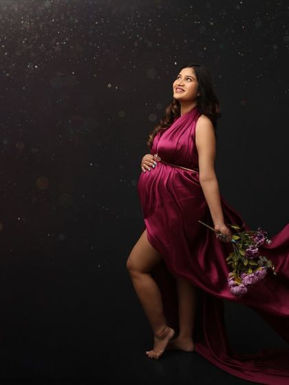 A dramatic and poetic portrait. The mom-to-be walks forward with a flowing magenta gown and a bouquet of flowers, looking up towards a hopeful, starry sky.