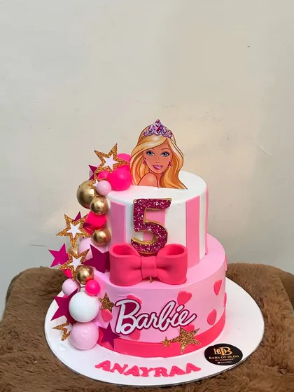 I bring popular themes to life with detailed, custom designs. This two-tiered Barbie cake for a 5th birthday features pink stripes, a sparkling number five, and a big fondant bow, creating a perfect centerpiece for a Barbie-themed party.