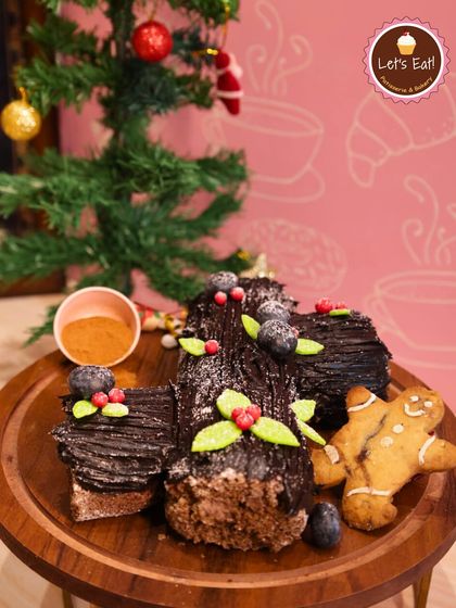 A classic Christmas Yule Log, decorated to resemble a festive log with chocolate bark, meringue mushrooms, and holly. It's a stunning and delicious addition to your Christmas table.