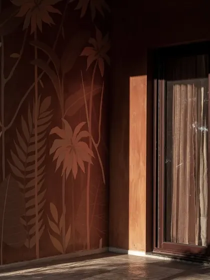 A detail of an exterior wall with a beautiful, tone-on-tone mural of tropical leaves. The morning light creates a soft, warm glow, highlighting the texture and artistry of the design.