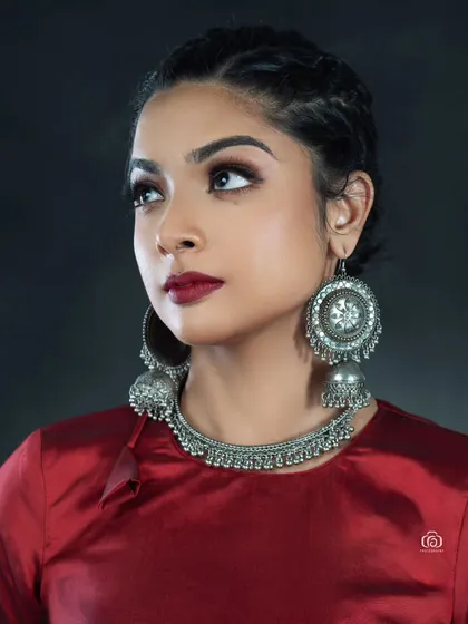 A close-up beauty shot focused on traditional silver jewelry. The rich red top and dark background make the intricate details of the earrings and necklace stand out.
