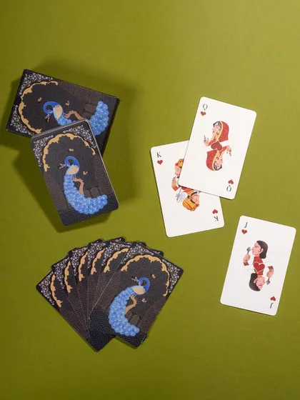 A flat lay of peacock-themed playing cards on a green background. The composition is balanced and clearly displays the unique design of the cards.