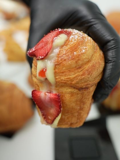 A student holds up a freshly baked strawberry cruffin. The flaky layers and creamy filling make this a highly addictive and popular treat.