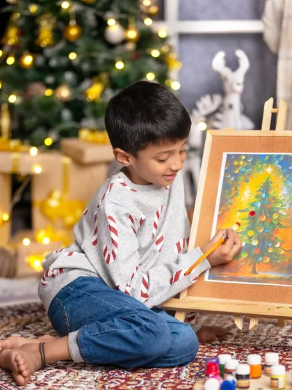 Christmas is about opening our hearts. A young boy is completely absorbed in painting a beautiful Christmas tree scene.