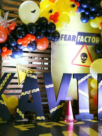 A close-up of the Fear Factor decor, showing the personalized "KAVIR" name blocks wrapped in caution tape and the skull and crossbones warning sign.