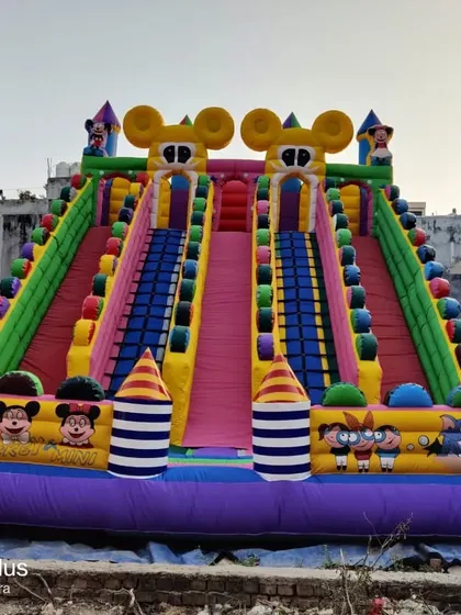 A big sliding bouncy with a Mickey Mouse theme and striped pillars, built with heavy-duty materials for commercial use.