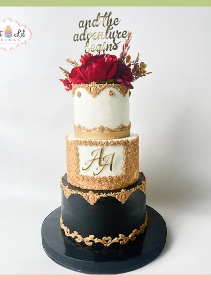 "And the adventure begins" with this bold and elegant three-tier wedding cake. Combining black, white, and shimmering gold with rich red florals, this design is perfect for couples looking for a sophisticated and modern statement piece for their special day.
