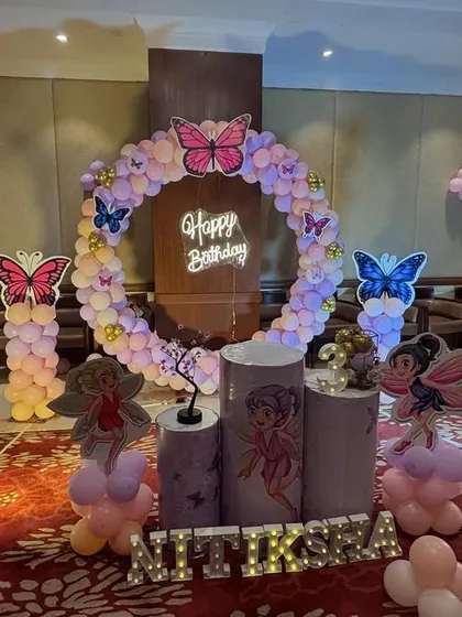 A grand butterfly-themed setup in a banquet hall. This decoration features a large balloon ring, multiple character and butterfly cutouts, and a light-up marquee number '3'.