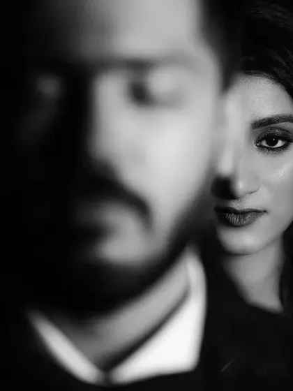 A moody black and white portrait with the groom's face blurred in the foreground, drawing focus to the bride's intense gaze.