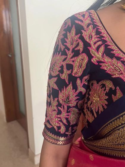 A close-up of the intricate pink and gold floral embroidery on the navy blue blouse sleeve.
