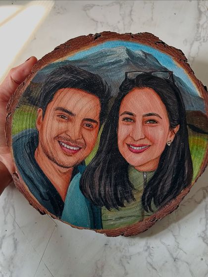 A hand-held view of a couple's portrait painted on a wood slice, set against a beautiful mountain landscape. These make for very personal and unique gifts.