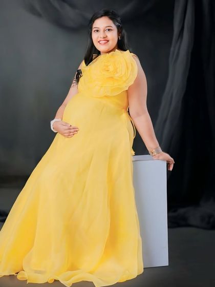 Shine bright in our yellow organza gown. The vibrant color and oversized statement flower create a cheerful and unforgettable look for your maternity photos.