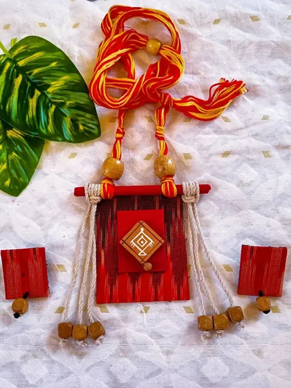 This is another angle of the red and yellow Ikat fabric necklace, clearly showing the hand-painted center, wooden beads, and the braided adjustable cord.