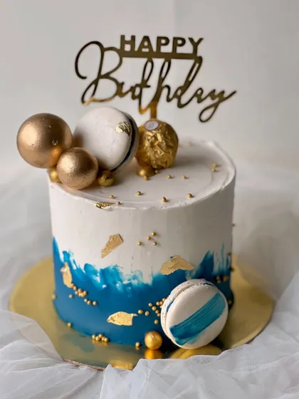 A stylish and masculine design perfect for him. This rich vanilla buttercream cake features a blue watercolor effect, gold leaf, macarons, and a Ferrero Rocher topper.