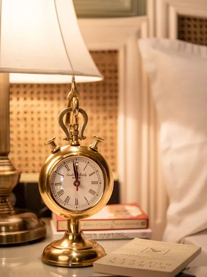 A vintage-style brass table clock on a bedside table. We create authentic lifestyle scenes to show how home decor items fit into a living space.