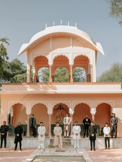 The groom's party, dressed in traditional attire, posing in front of a historic Rajasthani building, capturing the essence of a destination wedding.