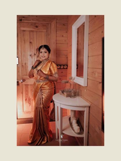 A bride in a golden saree, posing in a rustic, wood-paneled room.