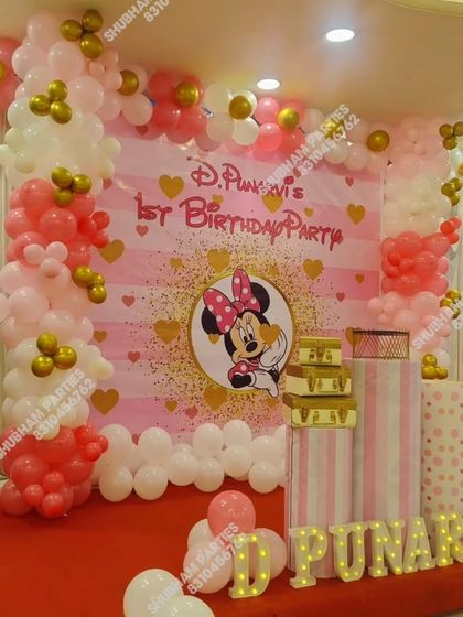A sweet Minnie Mouse first birthday party with a pink and gold theme, featuring a large backdrop and balloon columns.
