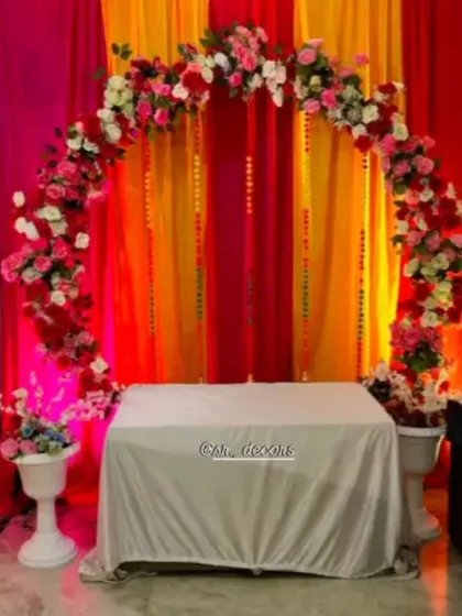 A beautiful floral ring backdrop is perfect for your Mehndi or Sangeet ceremony. This setup uses a mix of pink and white flowers against vibrant drapes to create a lively photo corner.