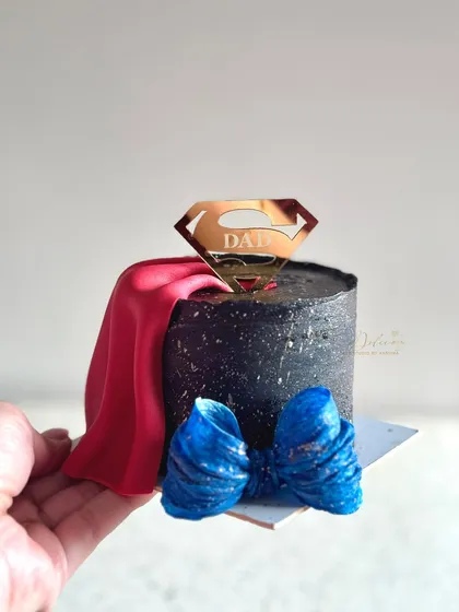 A handheld view of the Superman-themed bento cake. You can see the details of the fondant cape and bow tie, making it a fun and memorable cake for any dad.