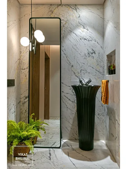 This powder room makes a bold statement with a freestanding black pedestal sink against a white marble wall. A full-length mirror and a modern pendant light add to the dramatic and stylish look.